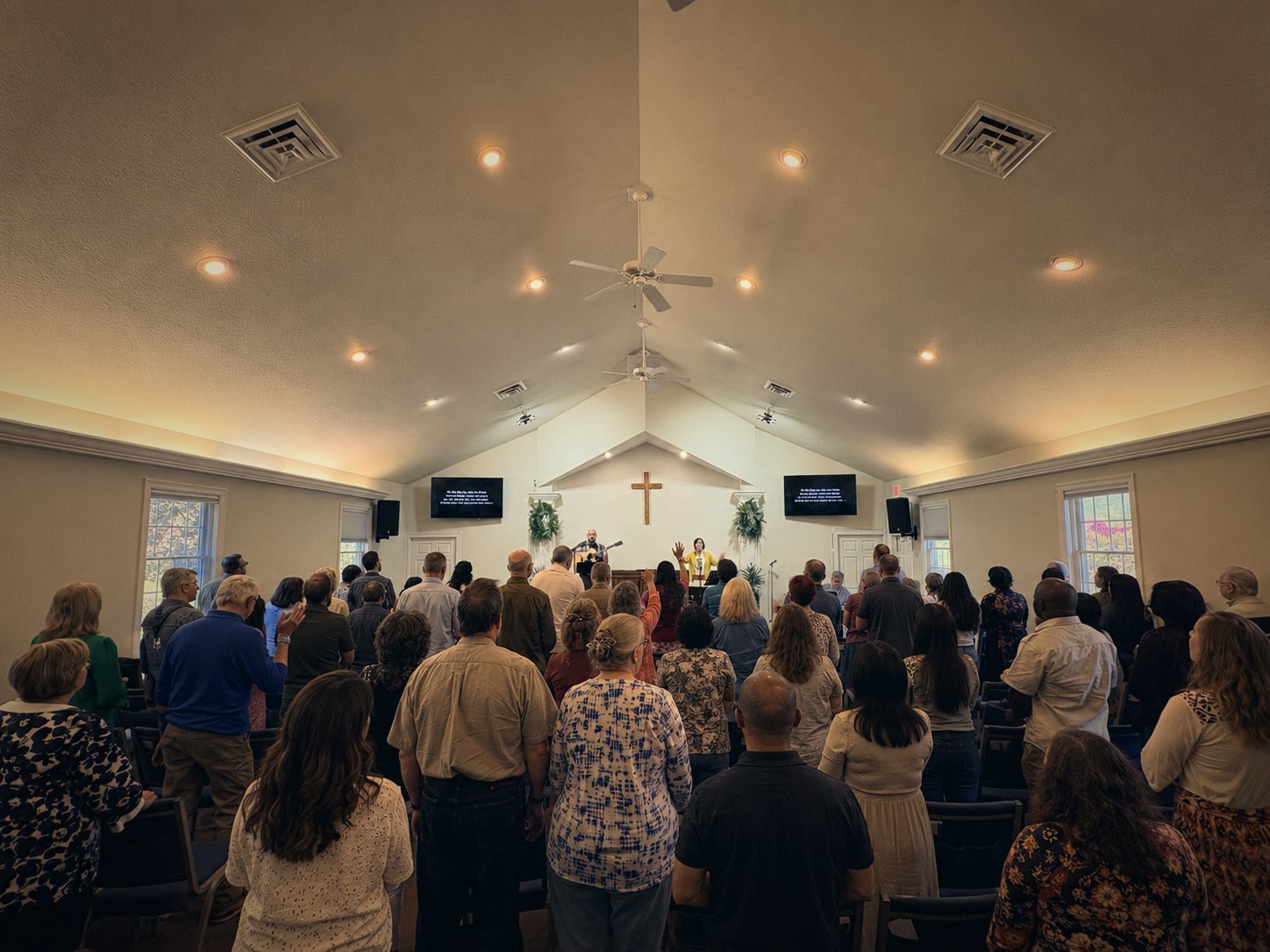 Ashe Alliance congregation standing together in worship — cross-centered sanctuary, warm Sunday morning light
